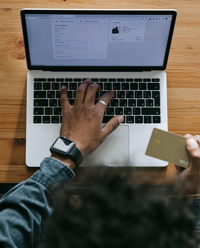 Person using a laptop to make an online purchase with a credit card on a wooden table.
